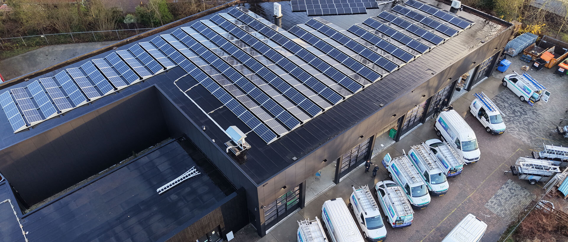 Luchtfoto van het ZPN pand met honderden zonnepanelen op het dak en het ZPN wagenpark ervoor